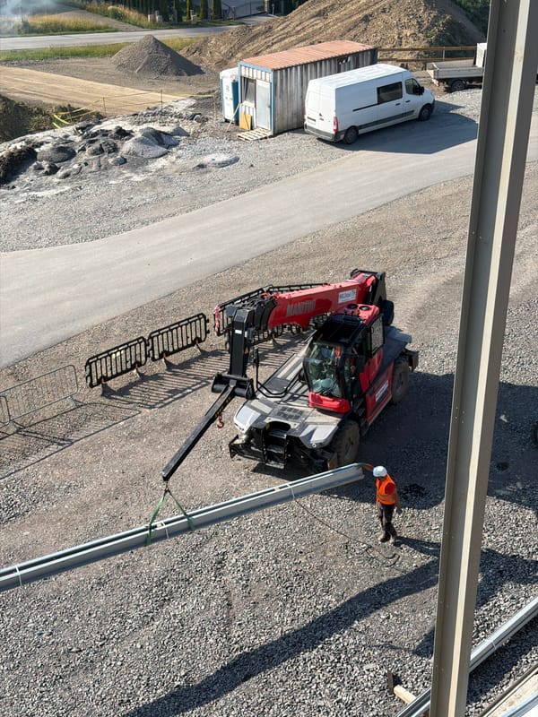 Hard-hatted worker handles wiring at a sunny Stróża construction site.