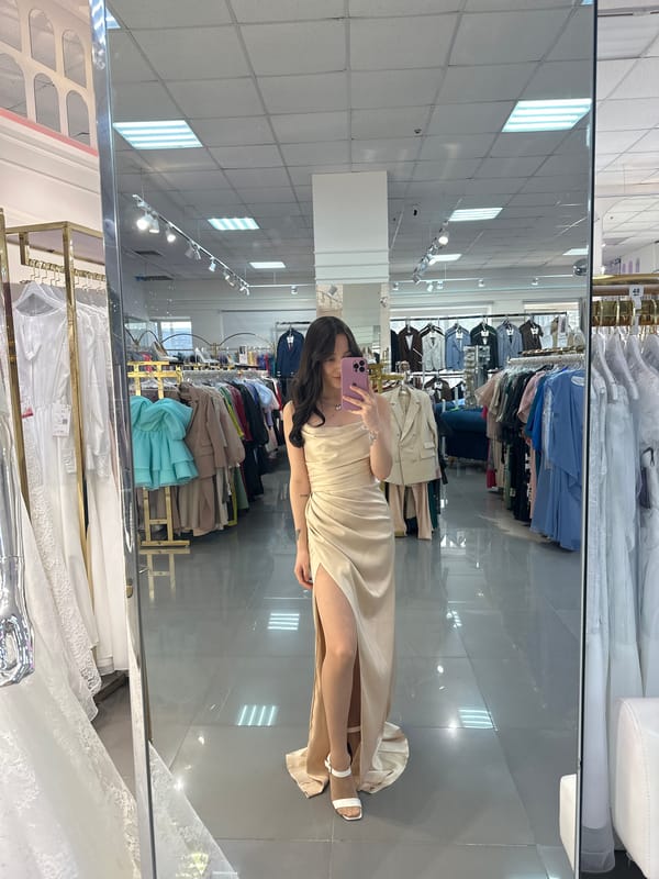 Woman takes mirror selfie in beige dress with pink phone