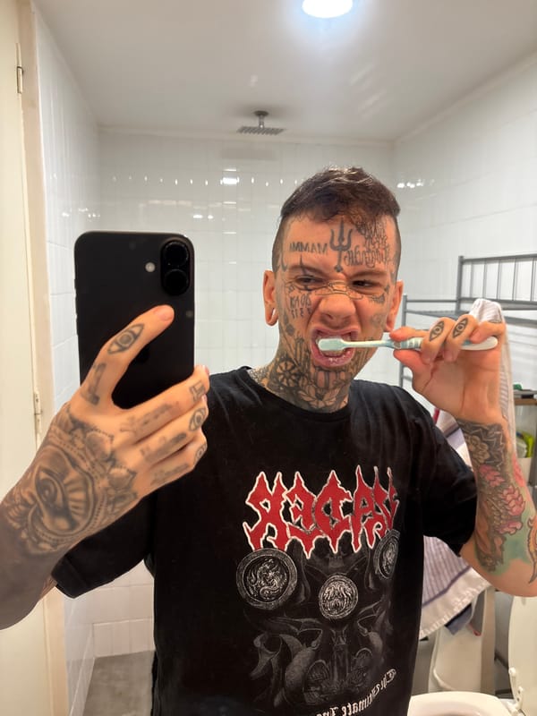 Tattooed person takes bathroom selfie while brushing teeth
