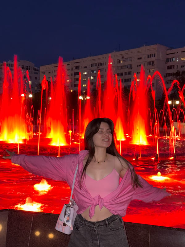 Woman poses at illuminated fountain during evening park visit