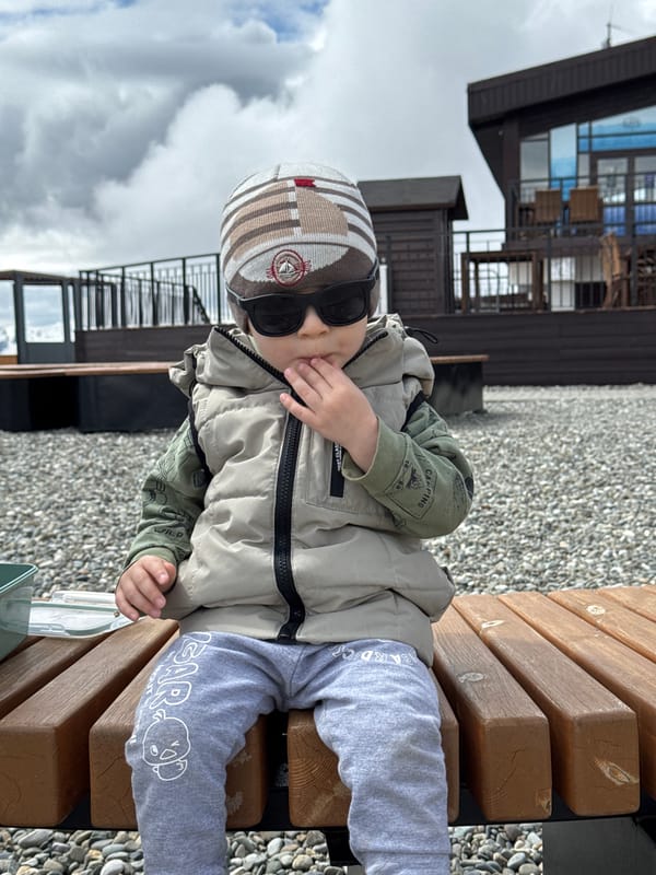 Toddler in sunglasses rests on wooden bench in Estosadok