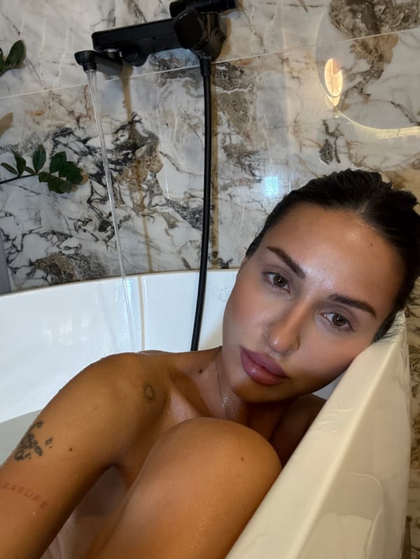 Woman photographed in bathroom with modern fixtures, tattoos visible