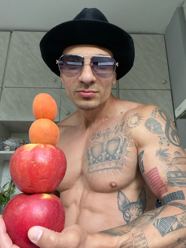 Tattooed, fedora-wearing figure poses in a Pleven kitchen