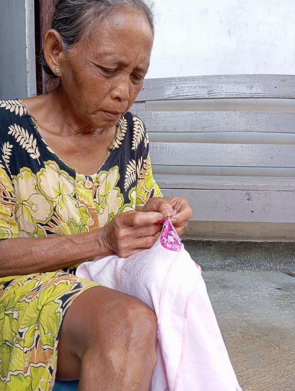 Elderly woman mends pink cloth outdoors in Baron, Indonesia