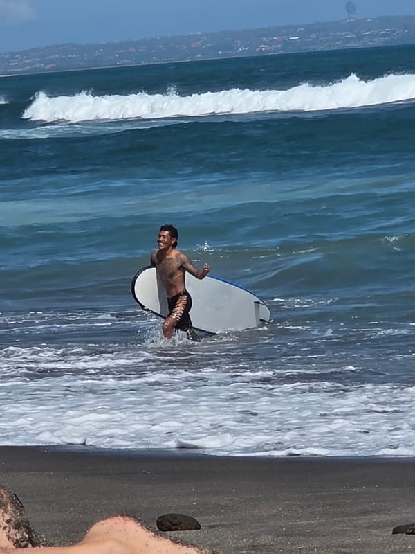 Morning at North Kuta's black sand beach: surfers, families, and shoreline views