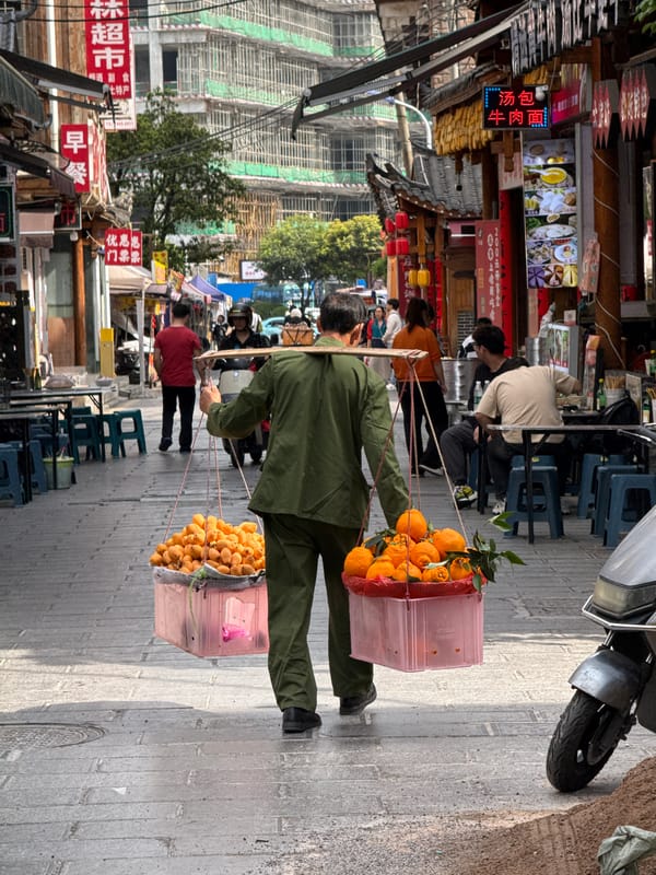 Man carries oranges in bins through Zhangjiajie streets