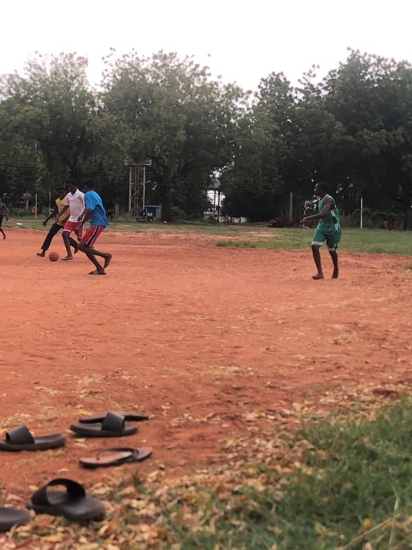 Young men play casual soccer on dirt field in Nigeria