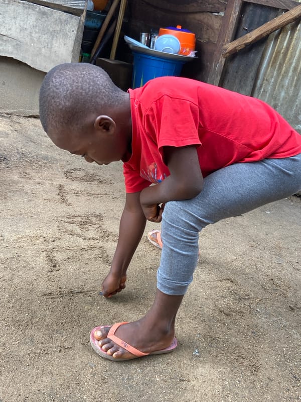 Child draws in dirt with stick in Mararaba, Nigeria