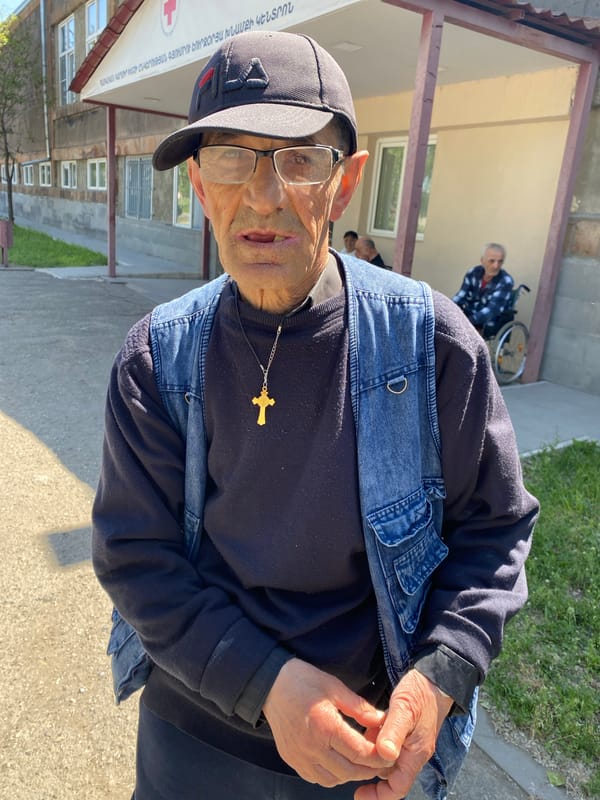 Denim vest and gold cross outside a Gyumri building