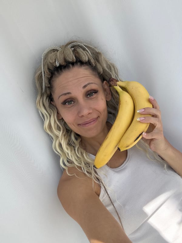 Woman poses with bananas while lying on white surface