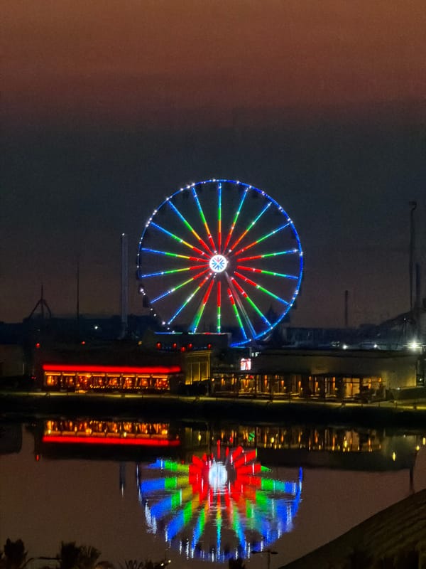 Lit Ferris wheel anchors a waterfront city at dusk