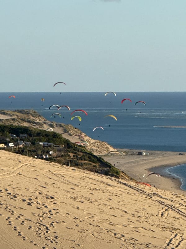 Evening visitors document Dune of Pilat's sandy slopes, paragliders