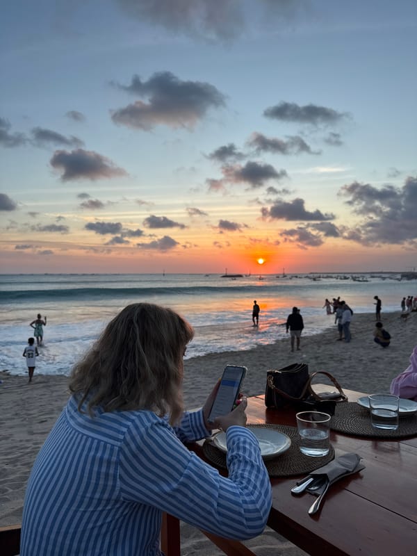 Woman uses phone at beach table during Kuta sunset