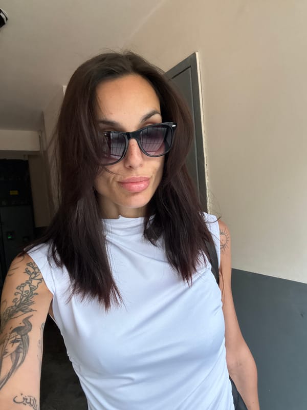 Tattooed woman in sunglasses observed against gray wall, Pleven