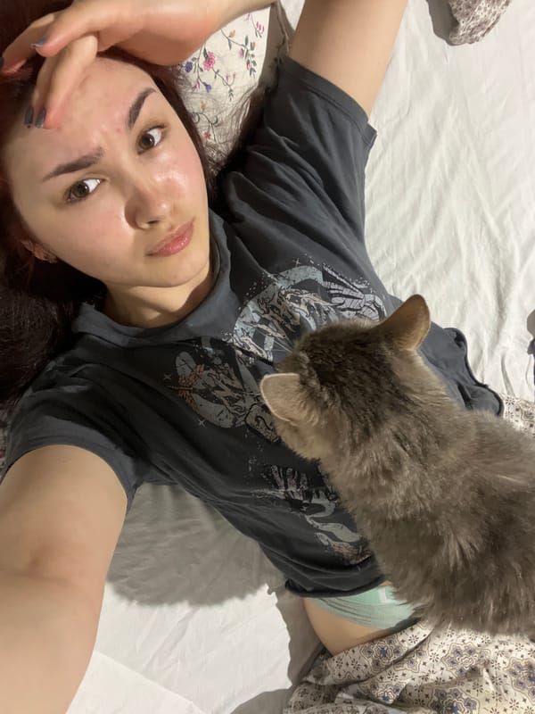 Woman poses with gray cat on bed in Neftekamsk