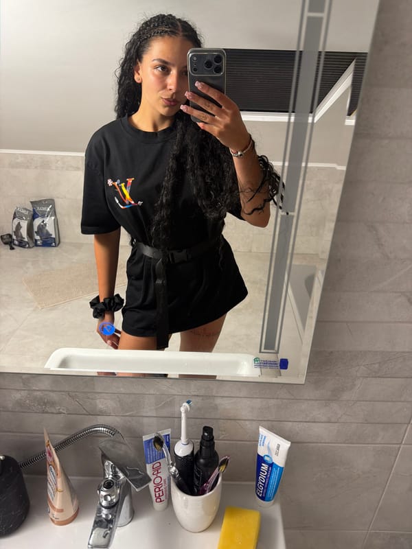 Mirror selfie session in a Gabrovo bathroom, graphic tee and braids.