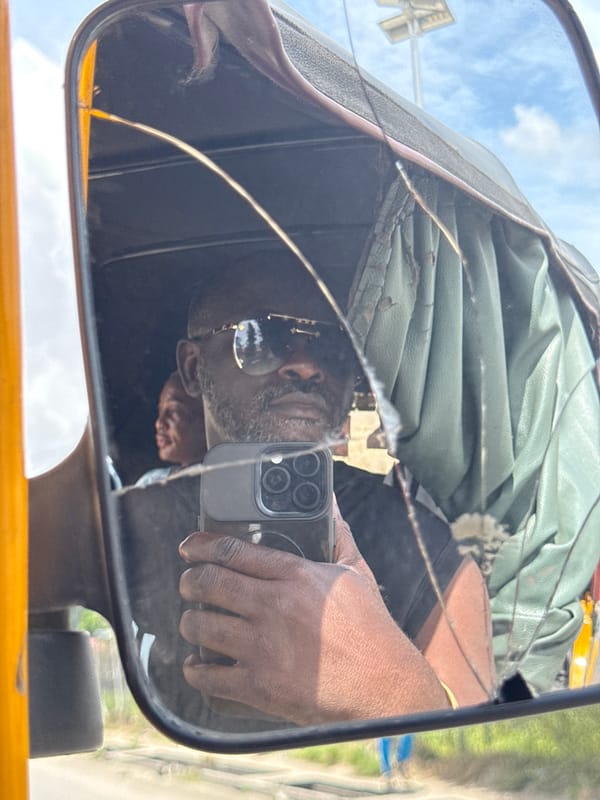 Cracked tricycle mirror reflects smartphone user in Ado, Nigeria