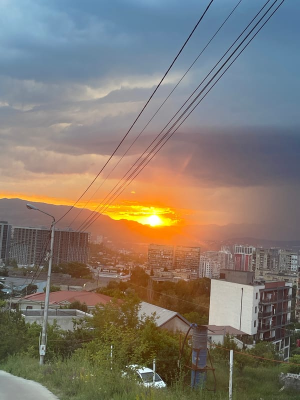 Sunset illuminates Tbilisi cityscape amid clouded evening skies