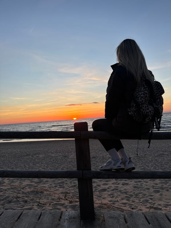 Woman watches Baltic Sea sunset from beach fence in Latvia