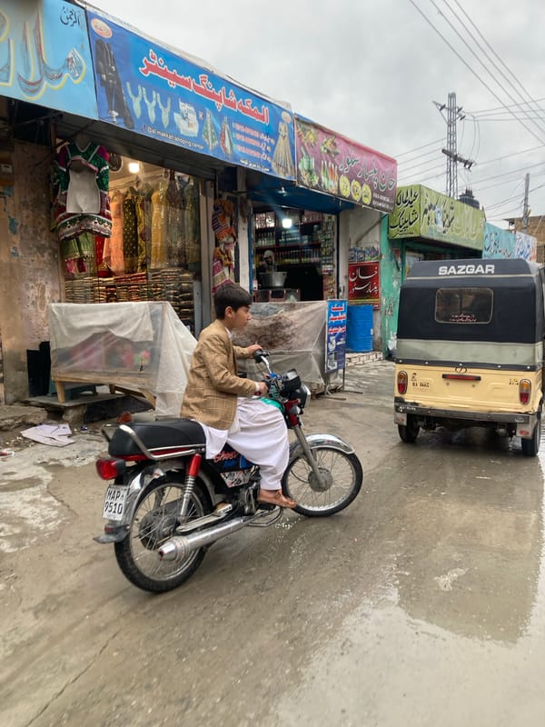 Boy sits on motorcycle near shop in Quetta