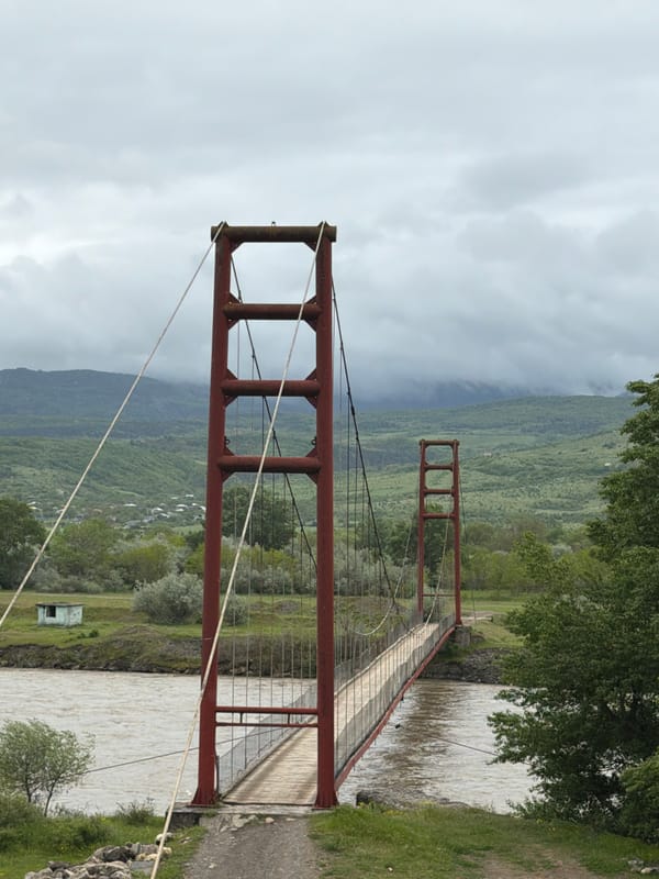 Red suspension bridge documented spanning river in Agarebi, Georgia