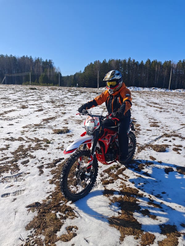 Dirt biker pauses on snowy field in sunny Прикамский
