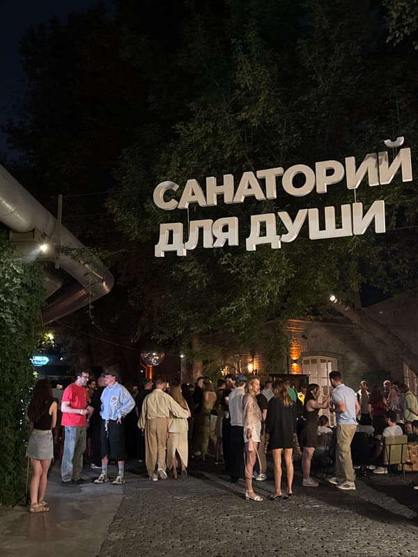 Evening crowd gathers under glowing Cyrillic letters at outdoor event