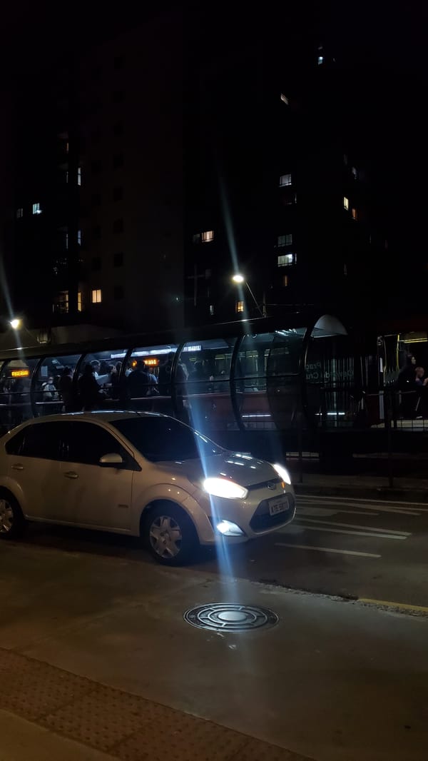 Commuters wait at glass bus shelter in Curitiba