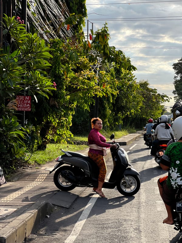 Woman sits on parked scooter in Denpasar street