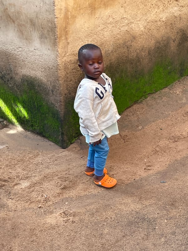 Kids playing near a mossy wall on a dirt path in rural Nigeria