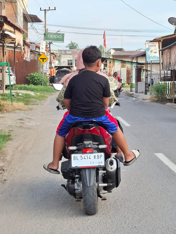 Man rides red moped through Keudegeudong, Indonesia
