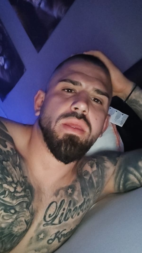 Tattooed man rests in blue-lit bedroom in Venlo