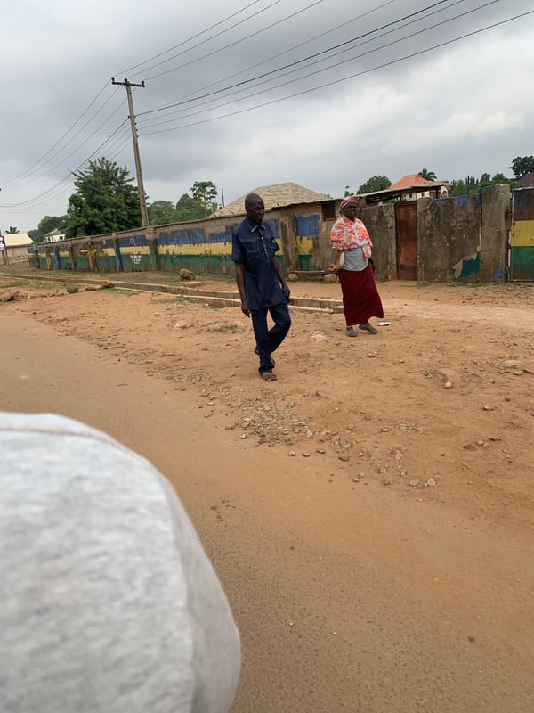 Two pedestrians walk dirt road in Maigizo, Nigeria