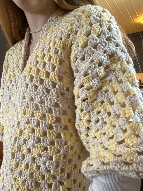 Woman showcases crocheted yellow sweater in Swedish kitchen