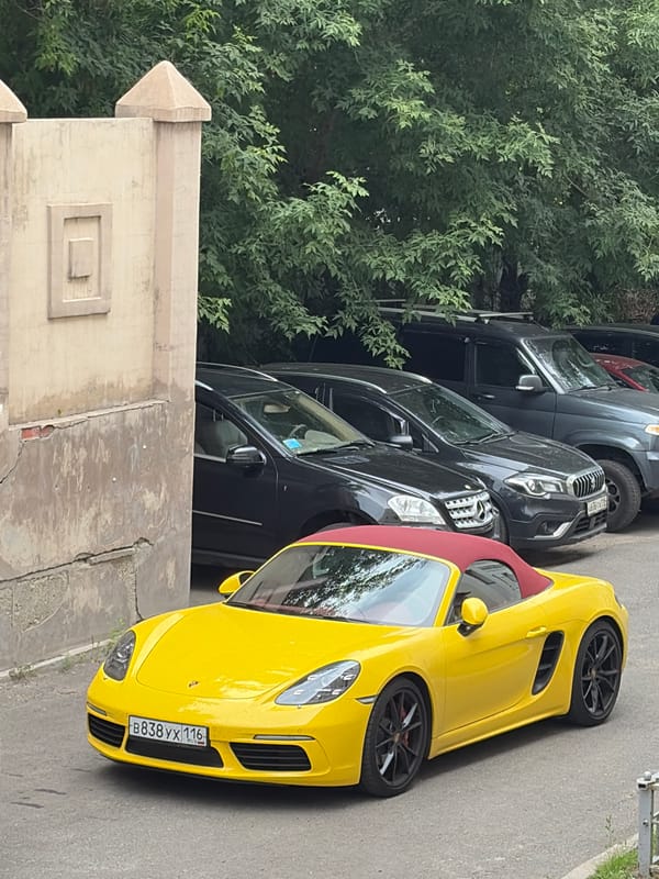 Yellow Porsche Boxster with red top parked on city street