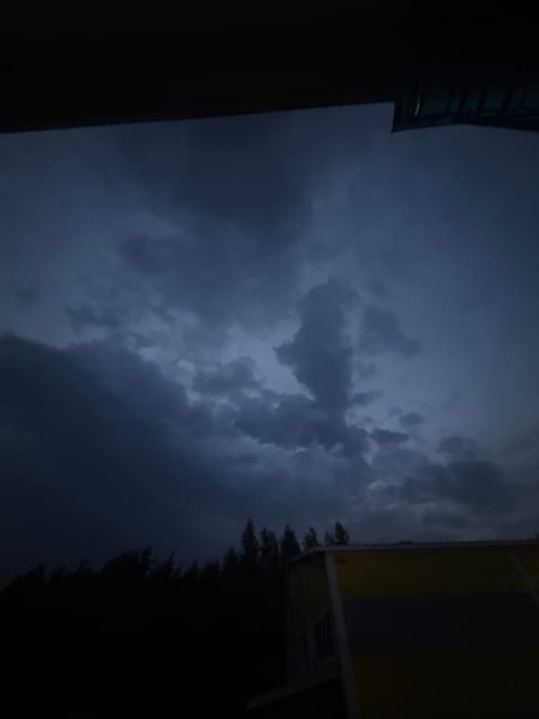Storm clouds gather at dusk over urban rooftops and a cell tower
