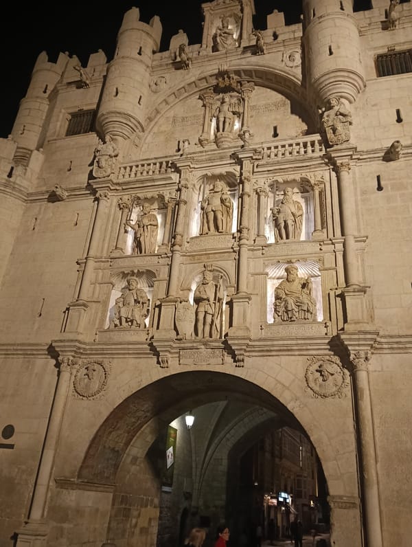 Uniformed marching band crosses street during nighttime procession in Burgos