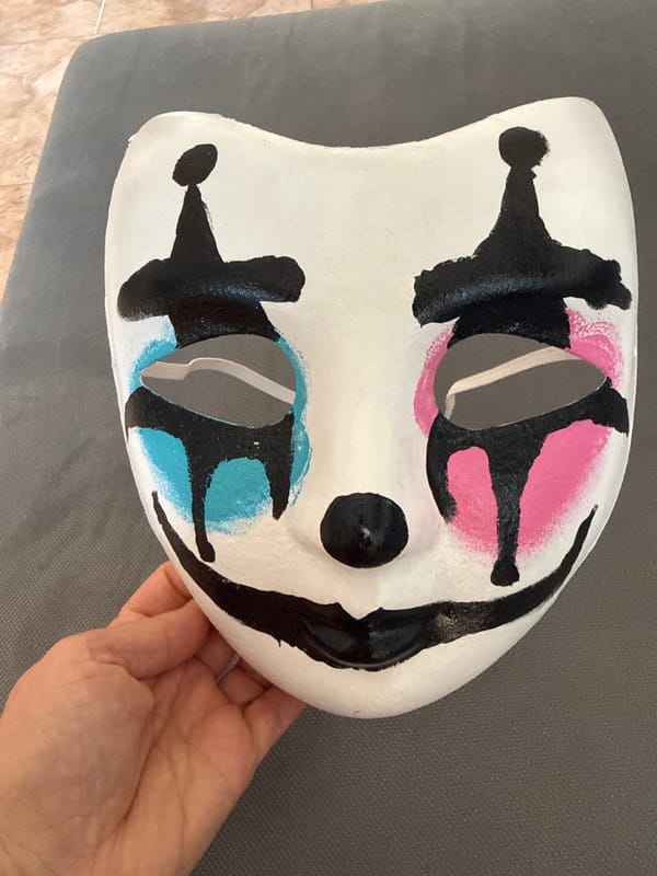 Person holds decorated white mask with colored markings