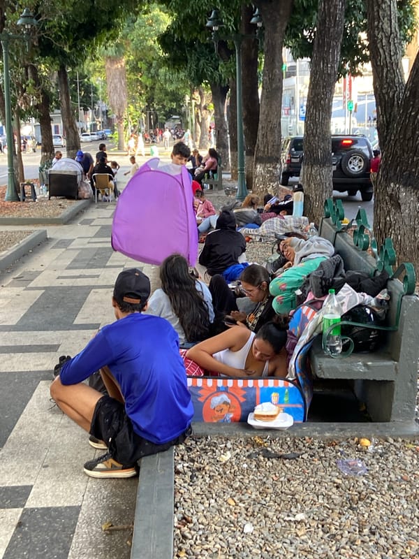 People resting and moving through a Caracas street at dusk