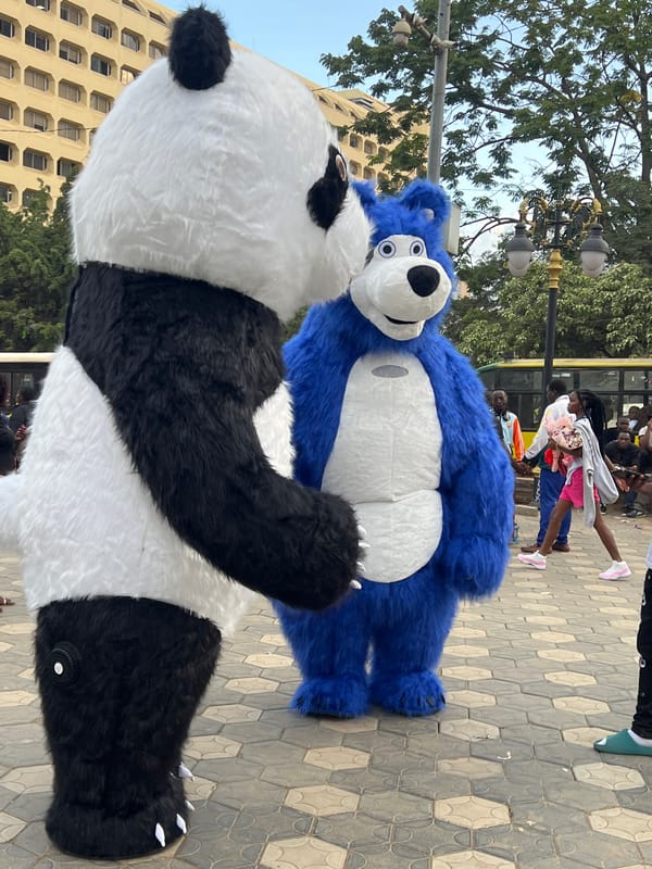 Street market bustles with vendors, food prep, mascots in Nairobi