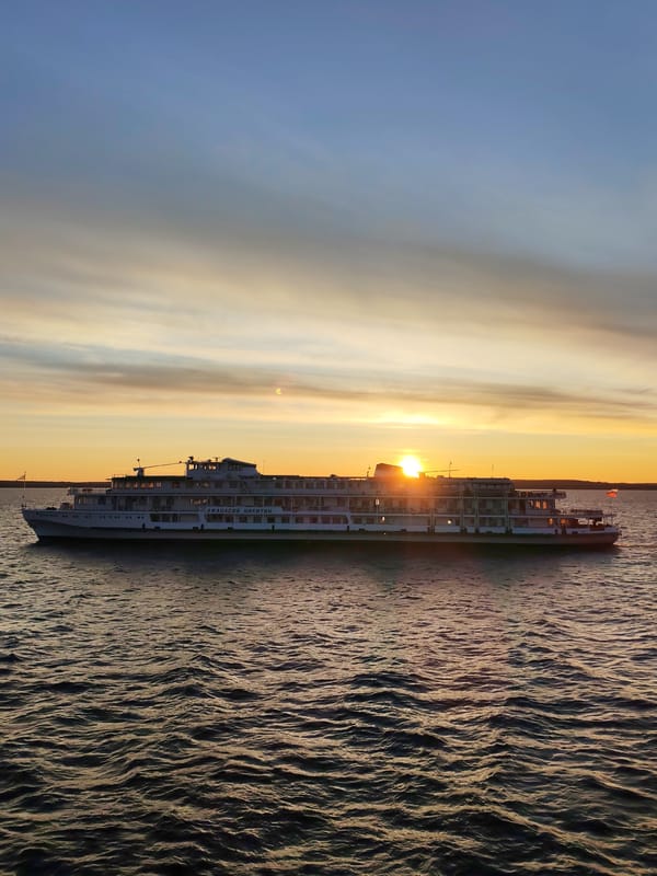 River cruise ship sails past Mikhalevo under sunset sky
