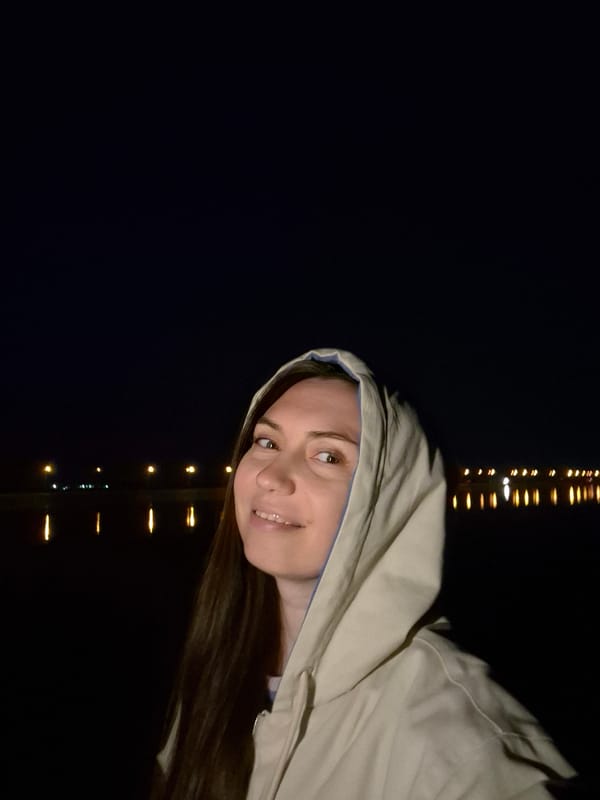 Woman in hooded jacket photographed smiling near yellow lights
