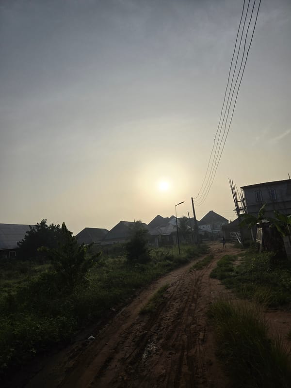 Morning haze obscures sun over dirt road to buildings