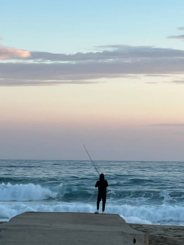 Lone angler fishes from Alanya embankment under colorful evening sky