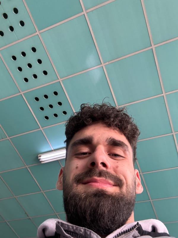 Man in gray hoodie takes selfie against tiled wall