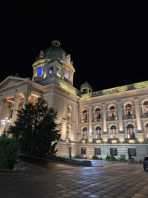 Night streets, lit monuments, and layered street art in a Balkan city