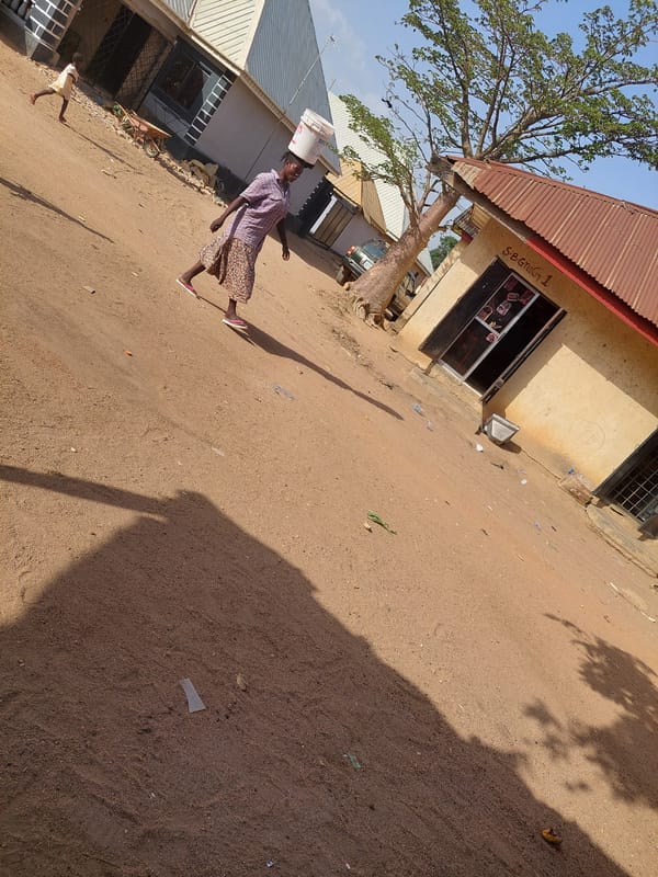 Woman carries water bucket on dusty Nigerian street