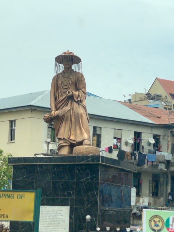 Street market bustles near bronze statue under overcast skies