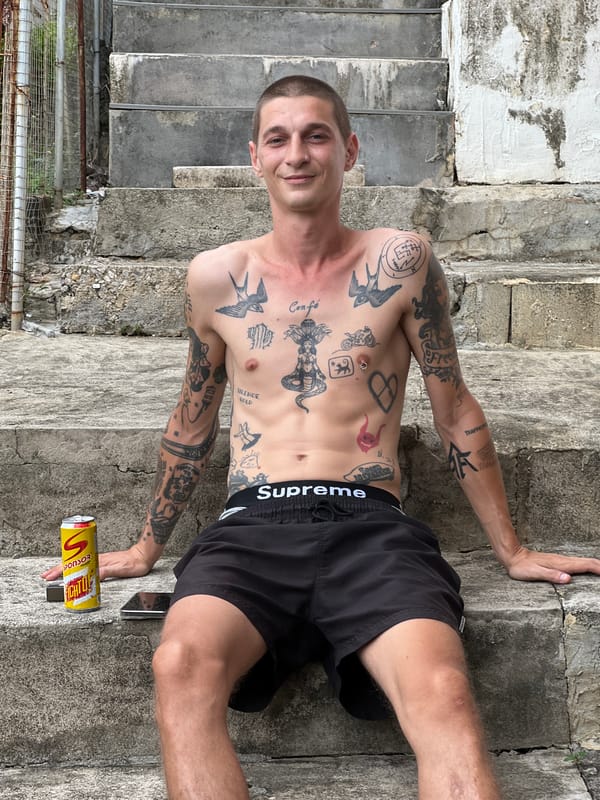 Tattooed and shirtless, phone in hand, chilling outside