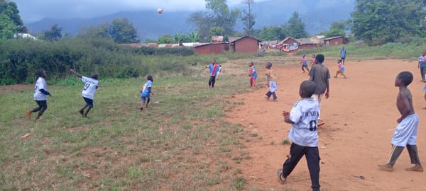 Children play soccer on dirt field in rural Congo